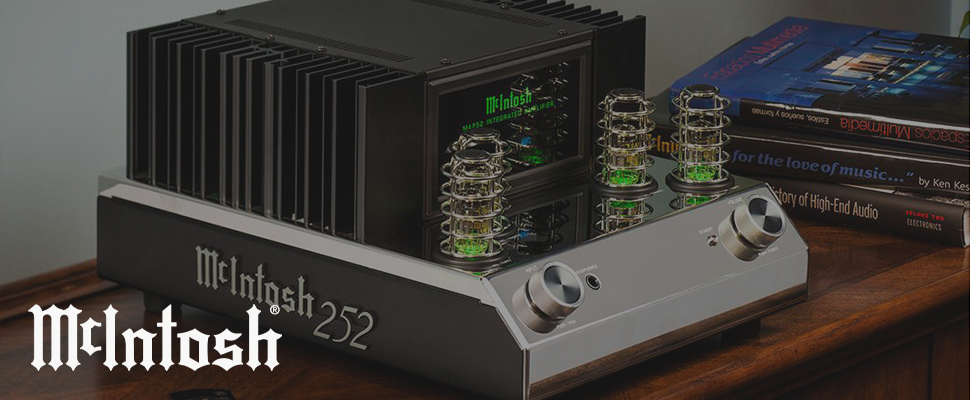 Close-up of a McIntosh audio amplifier with glowing tubes and green display, placed beside stacked books on high-end audio, creating a vintage, sophisticated atmosphere.