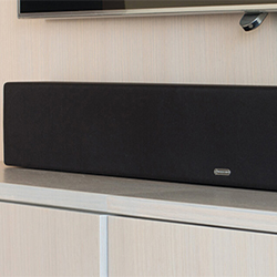 A sleek black soundbar is placed on a modern white shelf beneath a wall-mounted TV, conveying a minimalist and high-tech home entertainment setup.