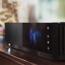 Modern black electronic device on a wooden surface, featuring a sleek design with a digital display showing colourful wave patterns and icons on the side.