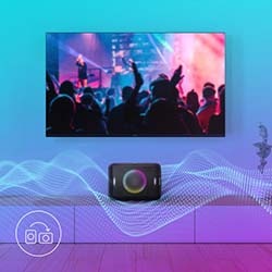A flat-screen TV displays a vibrant concert with cheering crowds. Below, a speaker emits colorful sound waves, creating a dynamic, energetic atmosphere.