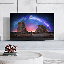 A sleek TV on a modern white stand displays a vivid image of a person standing between rock formations under a vibrant, starry night sky with a glowing arch.