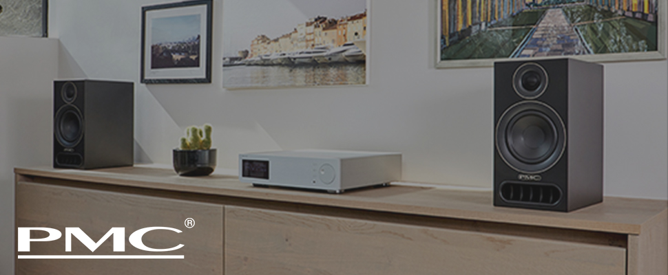 Two black PMC speakers stand on a stone wall background, showcasing sleek design and high-quality construction. PMC logo is visible on the left.