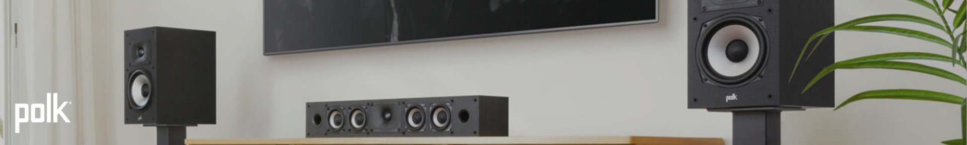 Modern living room with Polk audio speakers; two tall black speakers flank a central soundbar on a wooden console, creating a sleek, minimalistic setup.