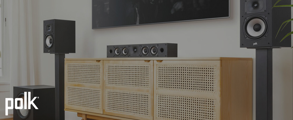 Modern living room with Polk audio speakers; two tall black speakers flank a central soundbar on a wooden console, creating a sleek, minimalistic setup.