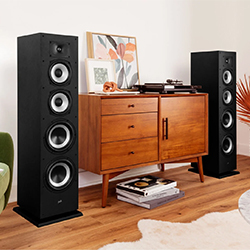 Room with a mid-century modern wooden cabinet, flanked by two tall black speakers. Décor includes framed art and stacked books. 