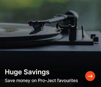 Vinyl turntable in focus with blurred green background. Text overlay reads "Huge Savings. Save money on Pro-Ject favourites" with an orange arrow.