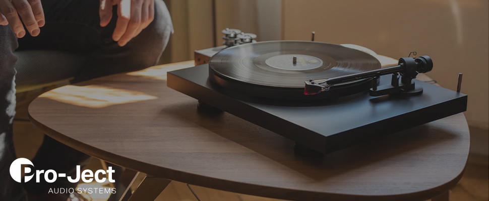 A vintage turntable with a spinning vinyl record sits in soft, warm lighting, conveying a nostalgic, relaxed atmosphere. The Pro-Ject Audio Systems logo is visible.