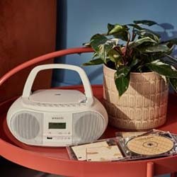 White boombox and CDs on a red table beside a potted green plant. The scene conveys a nostalgic and serene ambiance in a softly lit room.
