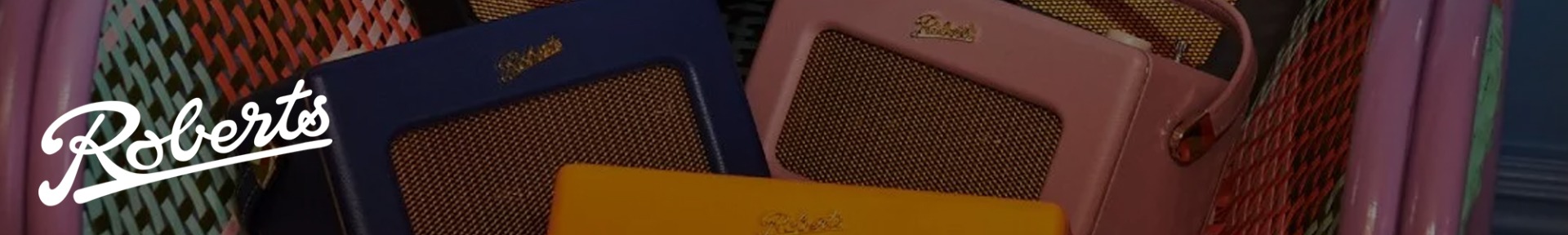 Colorful retro radios with mesh fronts are arranged in a pink basket. The brand name "Roberts" appears across several radios, exuding a vintage charm.