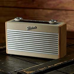 A vintage-style radio with a beige front and silver mesh grille. It has wood side panels, chrome knobs, and rests on a dark wooden surface, evoking nostalgia.