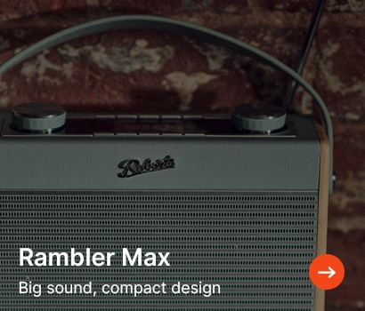 Grey radio with a vintage design, labelled "Rambler Max." It features large dials, set against a rustic brick wall, suggesting a retro vibe.