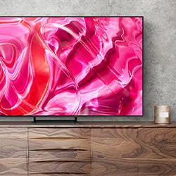A sleek, modern TV on a wooden cabinet displays vibrant pink and red abstract swirls. A small candle sits on the cabinet, set against a grey wall.