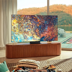 A vibrant abstract painting on a large flat-screen TV stands on a wooden cabinet in a cozy living room, with a scenic autumn view outside large windows.