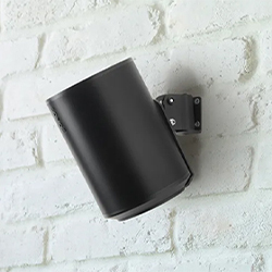A black outdoor wall light fixture is mounted on a textured white brick wall, angled downwards. The sleek design contrasts with the rustic backdrop.