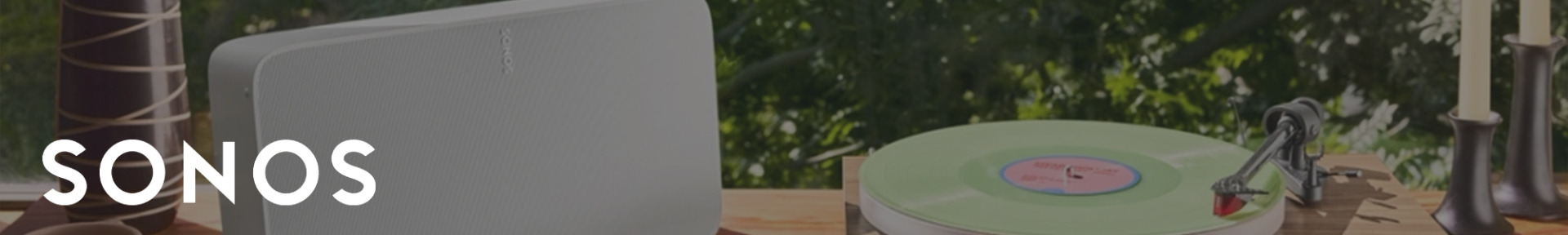 A Sonos speaker and a retro turntable with a green vinyl record sit on a wooden table. Sunlight filters through trees in the background, creating a serene ambience.