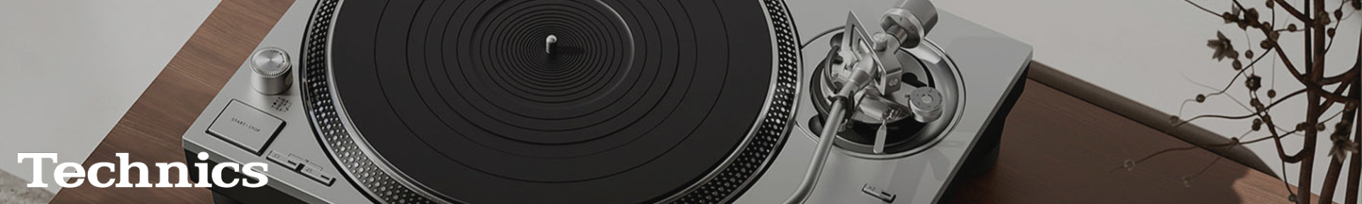 Turntable on a wooden table with a sleek silver tonearm and black platter. "Technics" text is visible; a minimalist, modern aesthetic is conveyed.