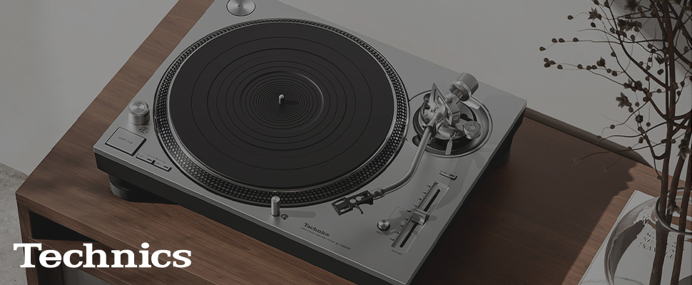 Turntable on a wooden table with a sleek silver tonearm and black platter. "Technics" text is visible; a minimalist, modern aesthetic is conveyed.