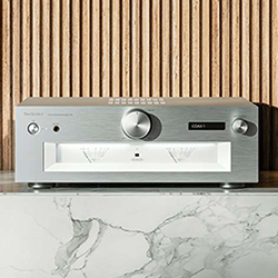 Sleek silver audio receiver with knobs and a digital display, set on a marble surface against a wooden slat background, conveying a modern aesthetic.