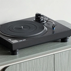 A modern black vinyl turntable sits on a wooden cabinet in a minimalistic setting. The tonearm is poised, evoking a sense of nostalgic elegance.