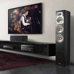 Living room with a large flat-screen TV showing a musician at a piano. A tall black speaker stands nearby, conveying a modern and artistic ambiance.
