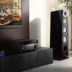 Modern home audio setup features a sleek black stereo system on a console, next to a tall speaker, with city lights visible through a window, conveying elegance.