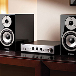 Yamaha audio system with two black speakers and a sleek amplifier on a wooden shelf, creating a modern, sophisticated ambiance.