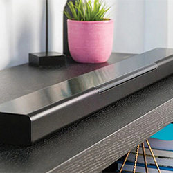A sleek black soundbar on a wooden shelf, next to a potted plant in a pink pot, conveying a modern and stylish home entertainment setup.