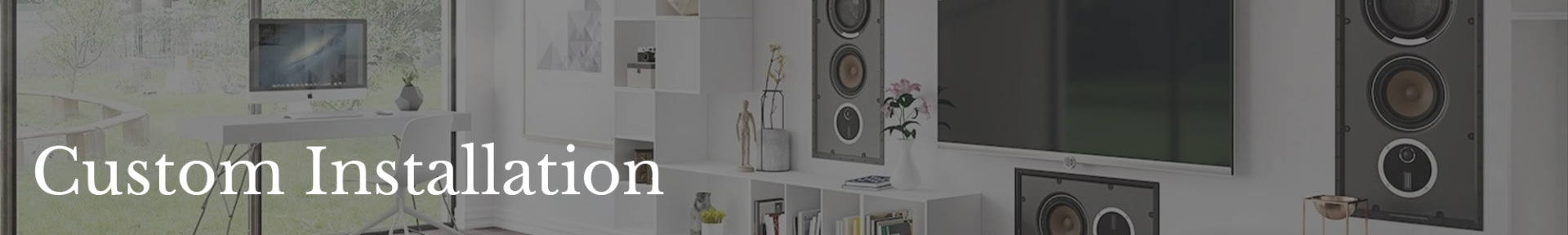Modern living room with large speakers, wall-mounted TV, and sleek furniture. Text "Custom Installation" overlaid. Bright, minimalist design.