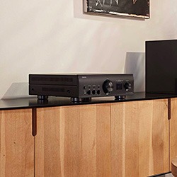 A black amplifier with knobs and buttons sits on a wooden console table in a modern room. 