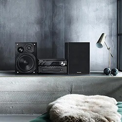 A sleek stereo system with speakers and receiver on a minimalist shelf, beside a modern lamp and soft fur throw, set against a concrete wall.