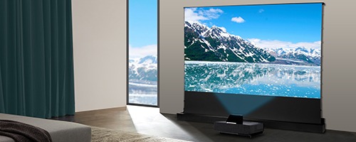 A modern living room features a large projector displaying snowy mountains and a lake, with natural light streaming through a nearby window.