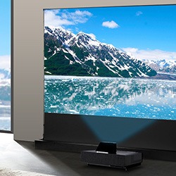 A modern living room features a large projector displaying snowy mountains and a lake, with natural light streaming through a nearby window.