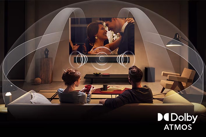 Dimly lit, cozy living room with a couple watching a movie on their LG OLED TV with LG Soundbar. Graphics show how Dolby Atmos fills the whole space with surround sound from all directions. Dolby Atmos logo is at the bottom corner. 