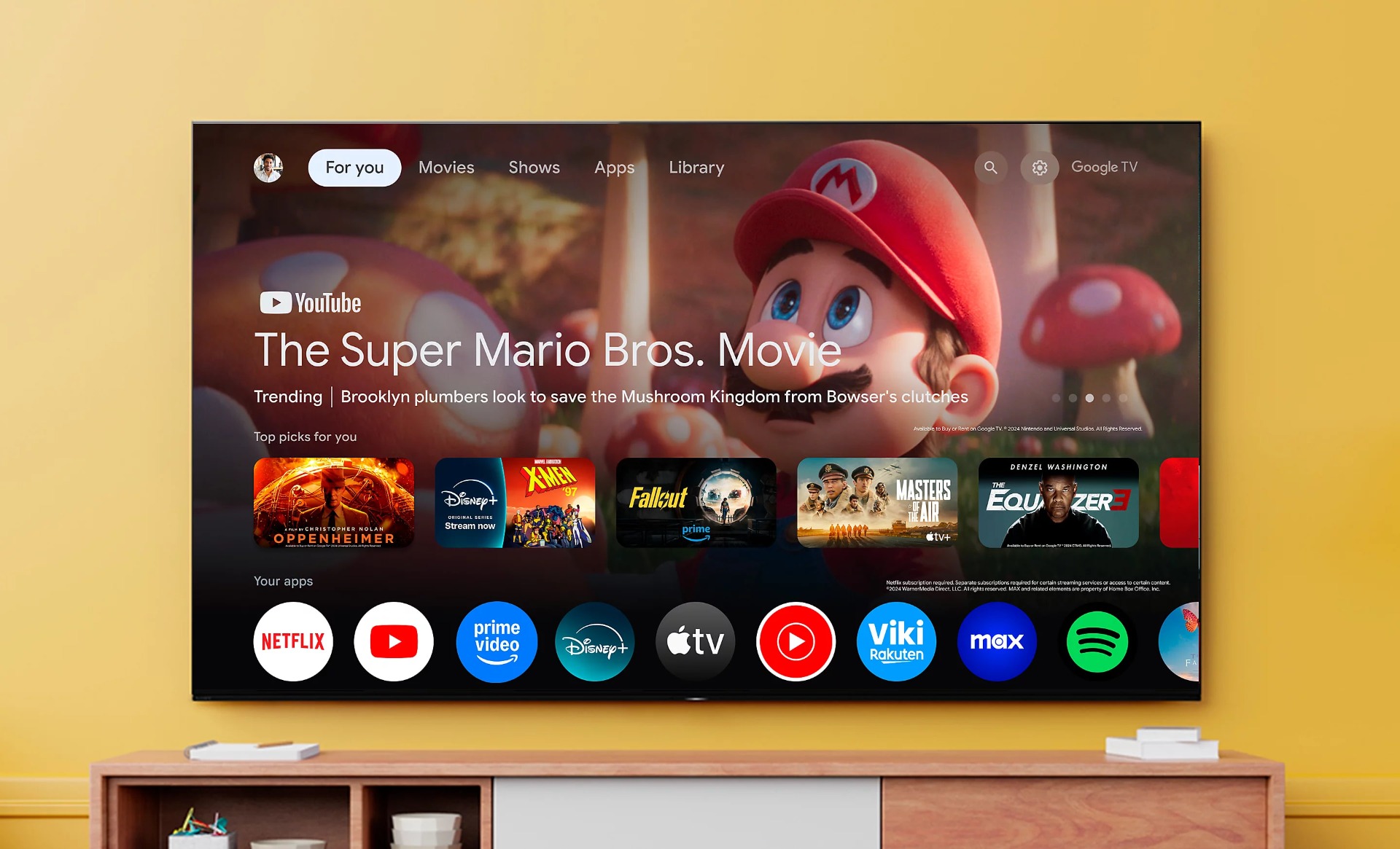 Large TV mounted on wall displaying Google TV interface, featuring The Super Mario Bros. Movie. Streaming apps shown below.