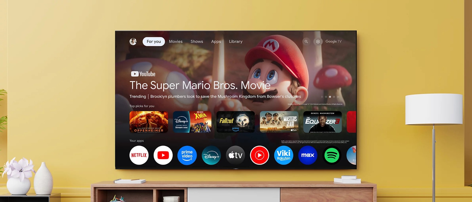 Wall-mounted TV displaying the Google TV home screen, featuring apps and movies.