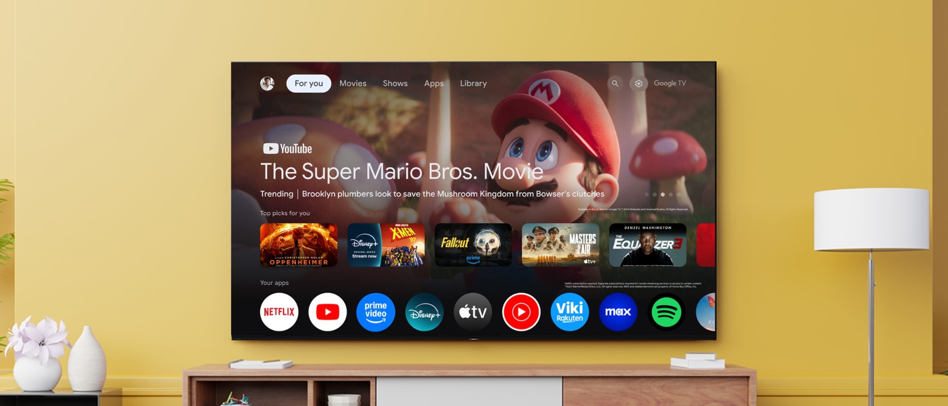 Large TV mounted on wall displaying Google TV interface, featuring The Super Mario Bros. Movie. Streaming apps shown below.