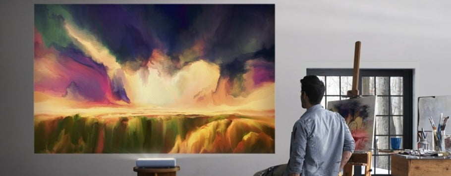 A person in a studio gazes at a vivid landscape painting with dramatic clouds and fields, evoking a sense of wonder. An easel and art supplies are nearby.