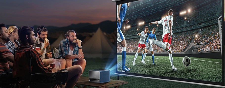 A group of people sitting outdoors, focused on a projected soccer match. The screen shows players mid-action in a stadium, creating an engaging and lively atmosphere.