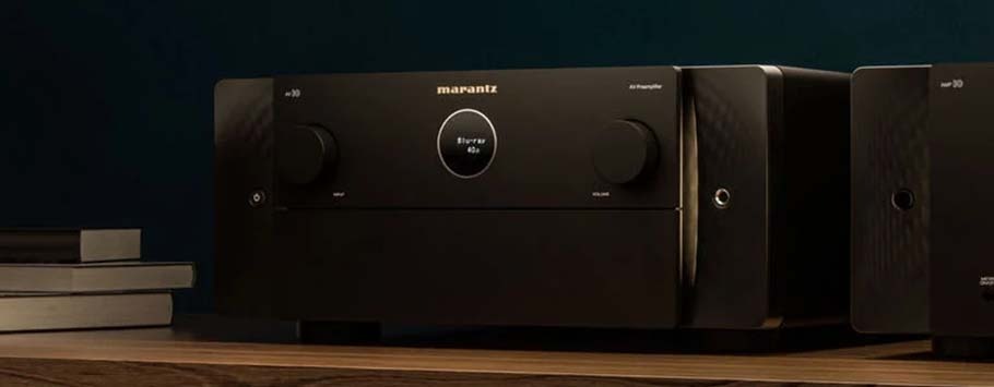 A sleek black audio amplifier with large knobs, centered on a wooden shelf beside books. The ambient lighting adds a sophisticated, modern feel.