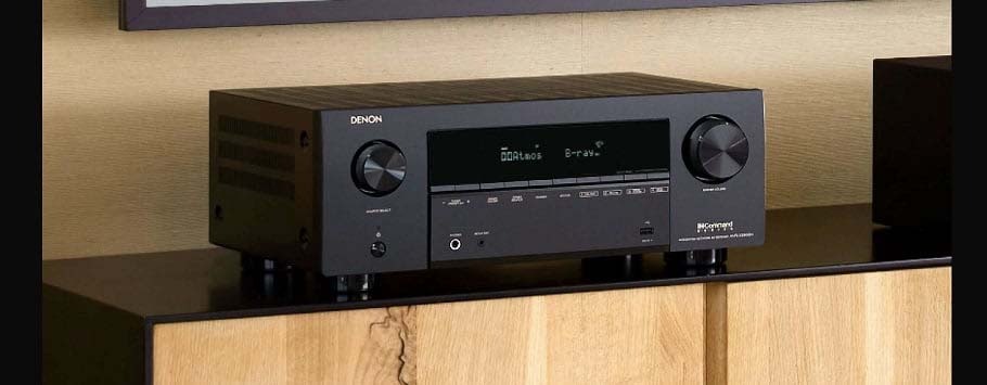 A sleek black audio receiver with digital display, large volume knobs, buttons, and ports on a wooden cabinet, creating a modern, sophisticated vibe.