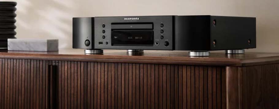A sleek black audio CD player sits atop a wooden cabinet with a modern, minimalist design. Soft lighting casts gentle shadows.