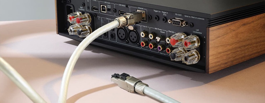 Rear view of an audio device with various input and output ports, including RCA connectors and Ethernet. A cable hangs mid-air, suggesting setup.