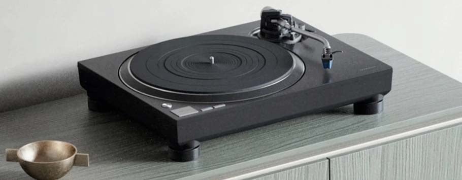 A sleek black turntable sits on a light gray wooden cabinet beside a small brass bowl.