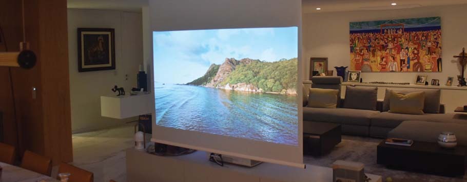 A serene coastal scene is projected onto a screen in a cosy living room, featuring a large sofa, vibrant artwork, and ambient lighting.