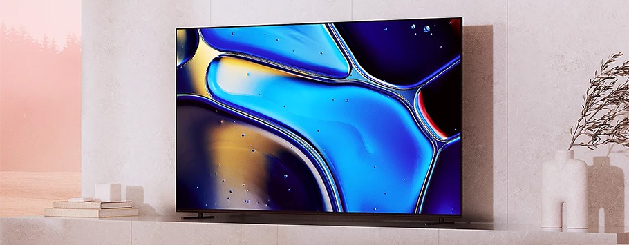 A sleek, modern TV on a light-coloured wall displays vibrant abstract blue and purple patterns. Minimalist décor includes stacked books and white vases.