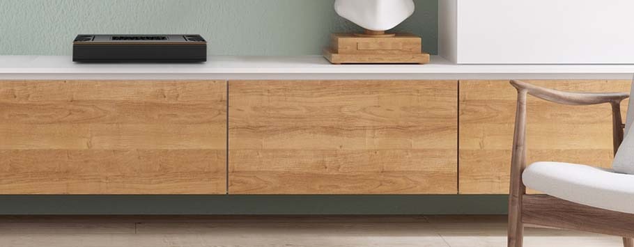 A modern living room with a sleek wooden sideboard with a Roon Server on it, jade green wall, and minimalist décor.