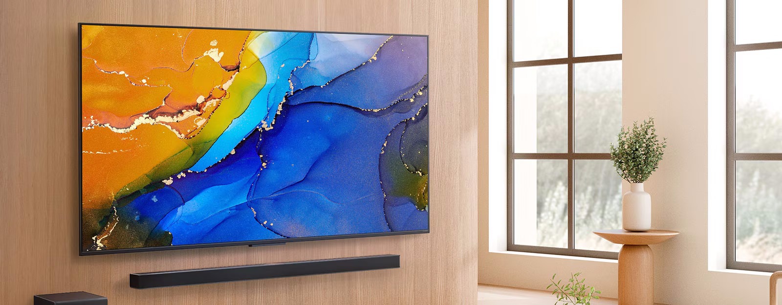 A modern TV mounted on a light wood wall displays vibrant abstract art in blue, orange, and yellow. Below is a black soundbar. A window and plant create a cosy, natural setting.