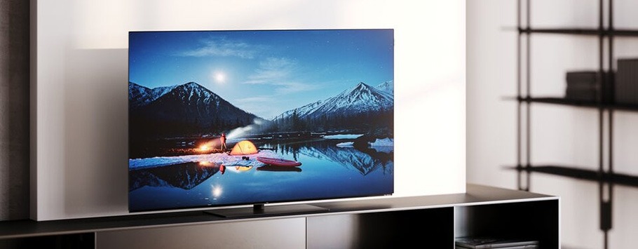 A sleek TV displays a serene campsite by a lake under a starry sky, with mountains in the background. The scene exudes tranquillity and nature's beauty.