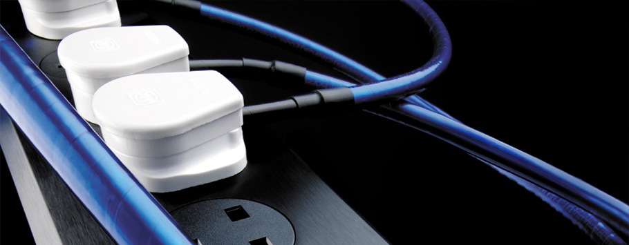 Close-up of white electrical plugs connected to a black power strip with blue cables, set against a dark background.