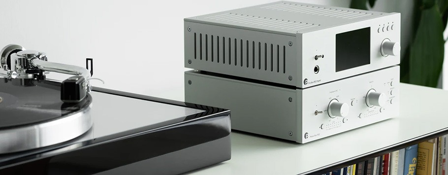 A modern turntable and a sleek, silver phono stage with knobs sit on a shelf.